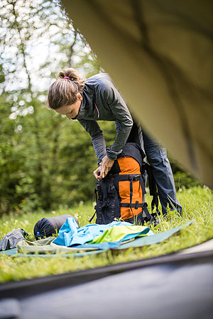 Bild zeigt in Detailaufnahme eine Frau beim Hantieren vor einem Zelt im Trekking-Camp