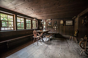 Stube im Hippenseppenhof mit Tisch, Stuhl, Bank und zahlreichen Kleinigkeiten an der Wand.