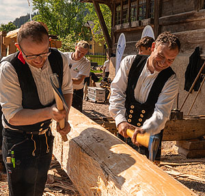 Zwei Zimmerleute beim Abbeilen eines Balkens